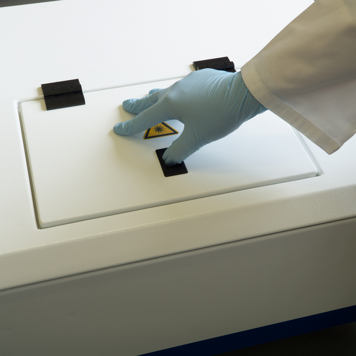 Hand in blauem Laborhandschuh öffnet den Deckel des weißen attomol Caleidoscan 100 Fluoreszenz-Imagers im Labor.