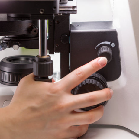 Hand bedient den Fokusknopf am ASKANIA Mikroskoptechnik ZEISS Primostar 3 Durchlichtmikroskop im Labor