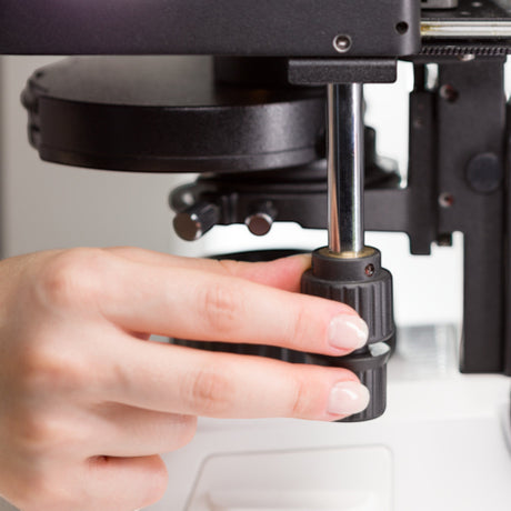 Hand bedient den Fokusknopf am ASKANIA Mikroskoptechnik ZEISS Primostar 3 Trino für präzise Scharfeinstellung
