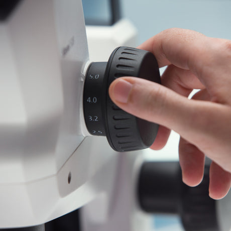 Hand bedient den Zoom-Drehknopf am ASKANIA Mikroskoptechnik ZEISS Stemi 508 Trino Stereomikroskop für präzise Analysen